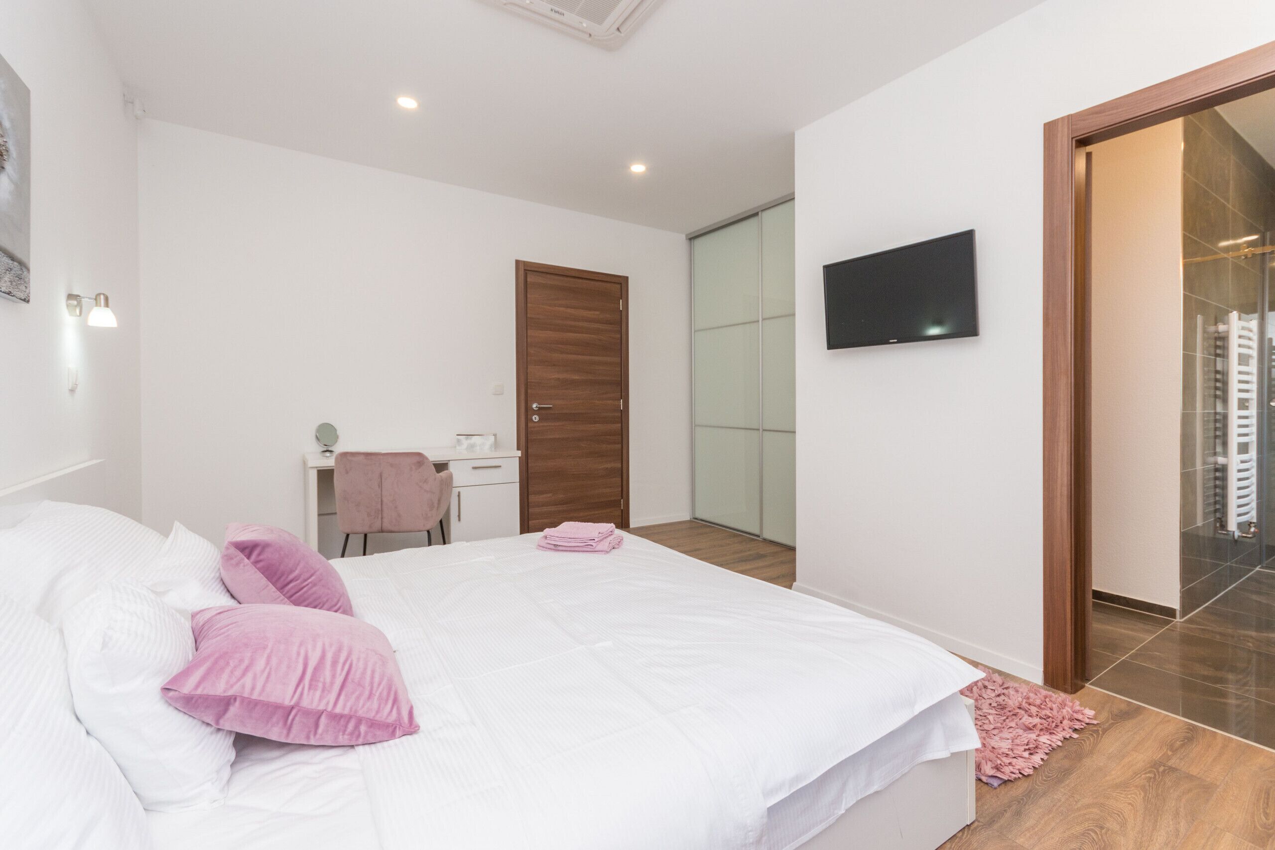 Une chambre à coucher comprenant un lit, un bureau, une chaise, un téléviseur et une porte vitrée donnant sur une salle de bain.