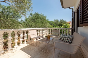 A balcony with a white railing, a table, two chairs, and a sofa.