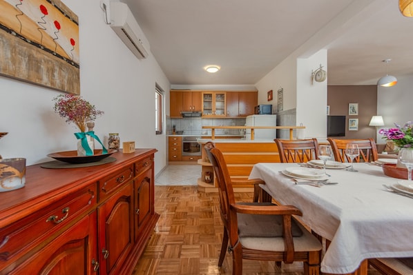 A dining area with wooden furniture, a kitchen in the background, and a painting on the wall.