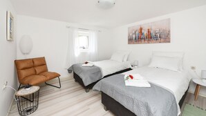Ein Hotelzimmer mit zwei Betten, einem braunen Sessel, einem kleinen runden Tisch und einem Stadtbild an der Wand.