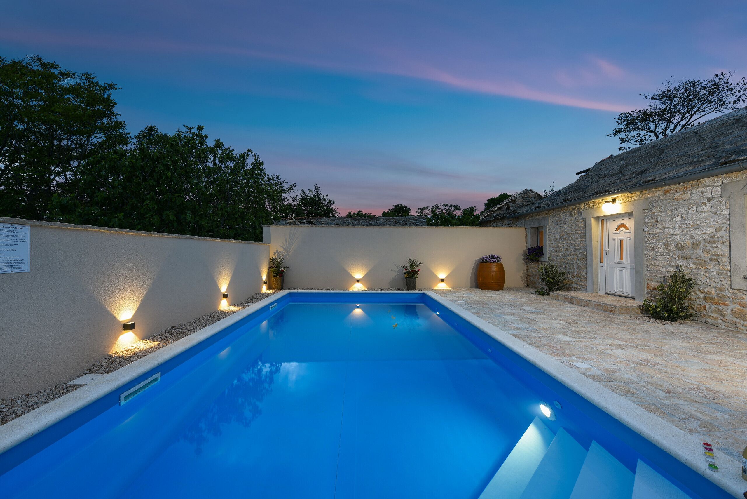 A swimming pool with stone walls and a stone building with a door.