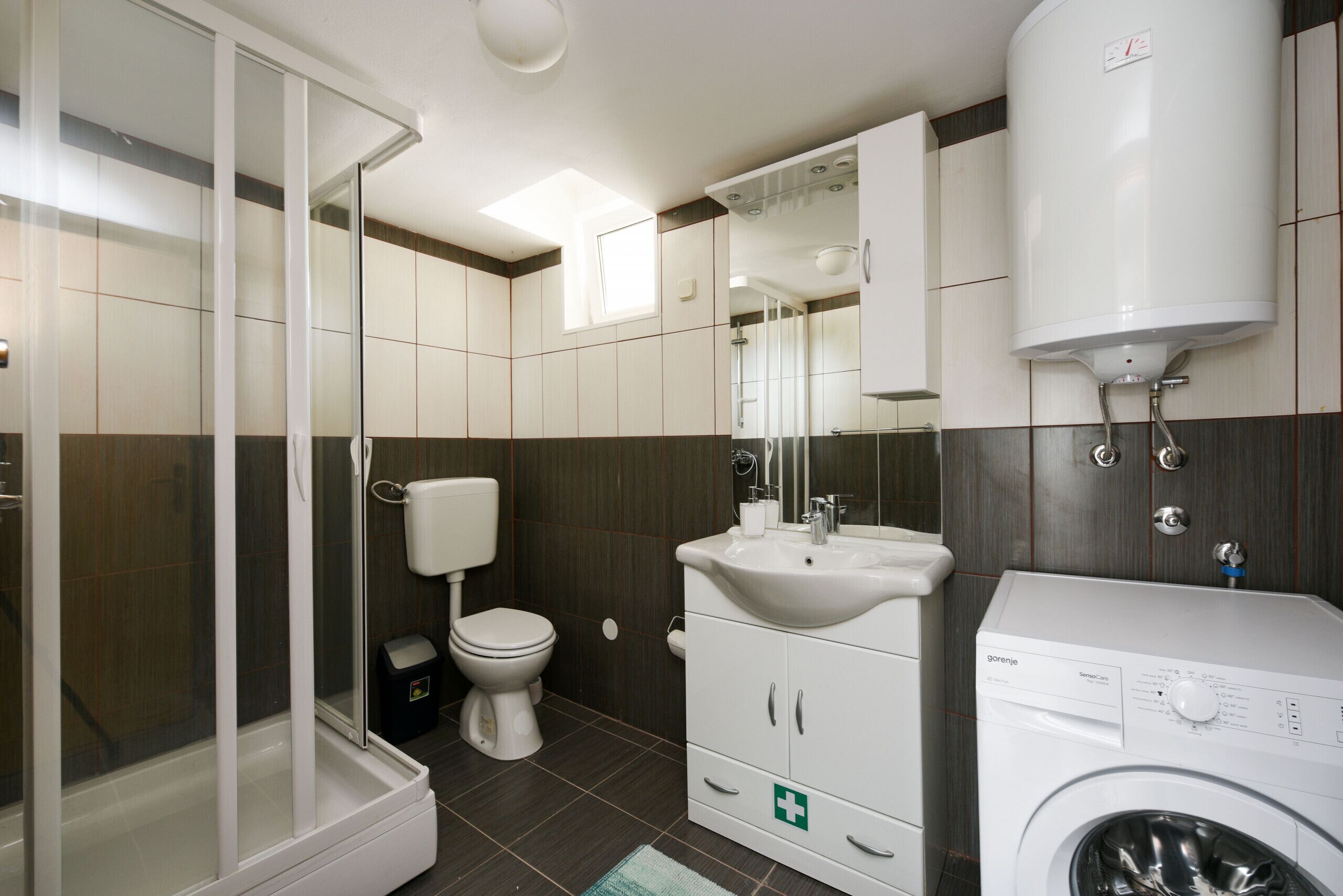Ein modernes Badezimmer mit Duschkabine aus Glas, Toilette, Waschbecken und Waschmaschine.