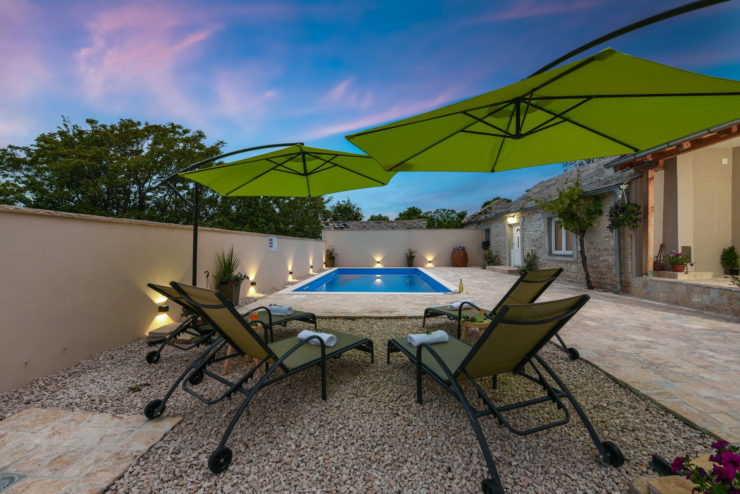 A pool area with four lounge chairs and two green umbrellas.
