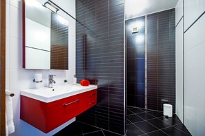 Un baño moderno con un tocador rojo, un lavabo blanco y un espejo grande.