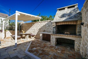 An outdoor patio with a stone fireplace, a wooden table, and a covered seating area. - Villa Castelo Coza (Posedarje)