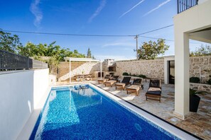 A swimming pool with lounge chairs and a stone wall. - Villa Castelo Coza (Posedarje)