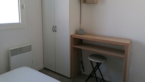 Un dormitorio con un armario blanco, un escritorio de madera, un taburete y una mesita de noche.