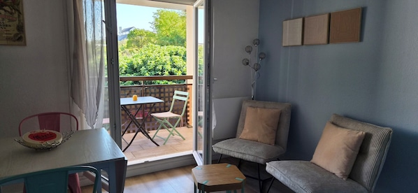Une pièce comprenant une table, des chaises, une petite table d’appoint, un canapé et donnant sur un espace verdoyant.