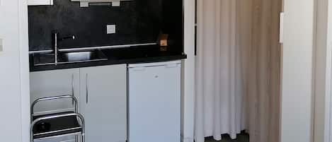 A compact kitchen with white cabinets, a black countertop, a microwave, a sink, a small refrigerator, and a metal cart.