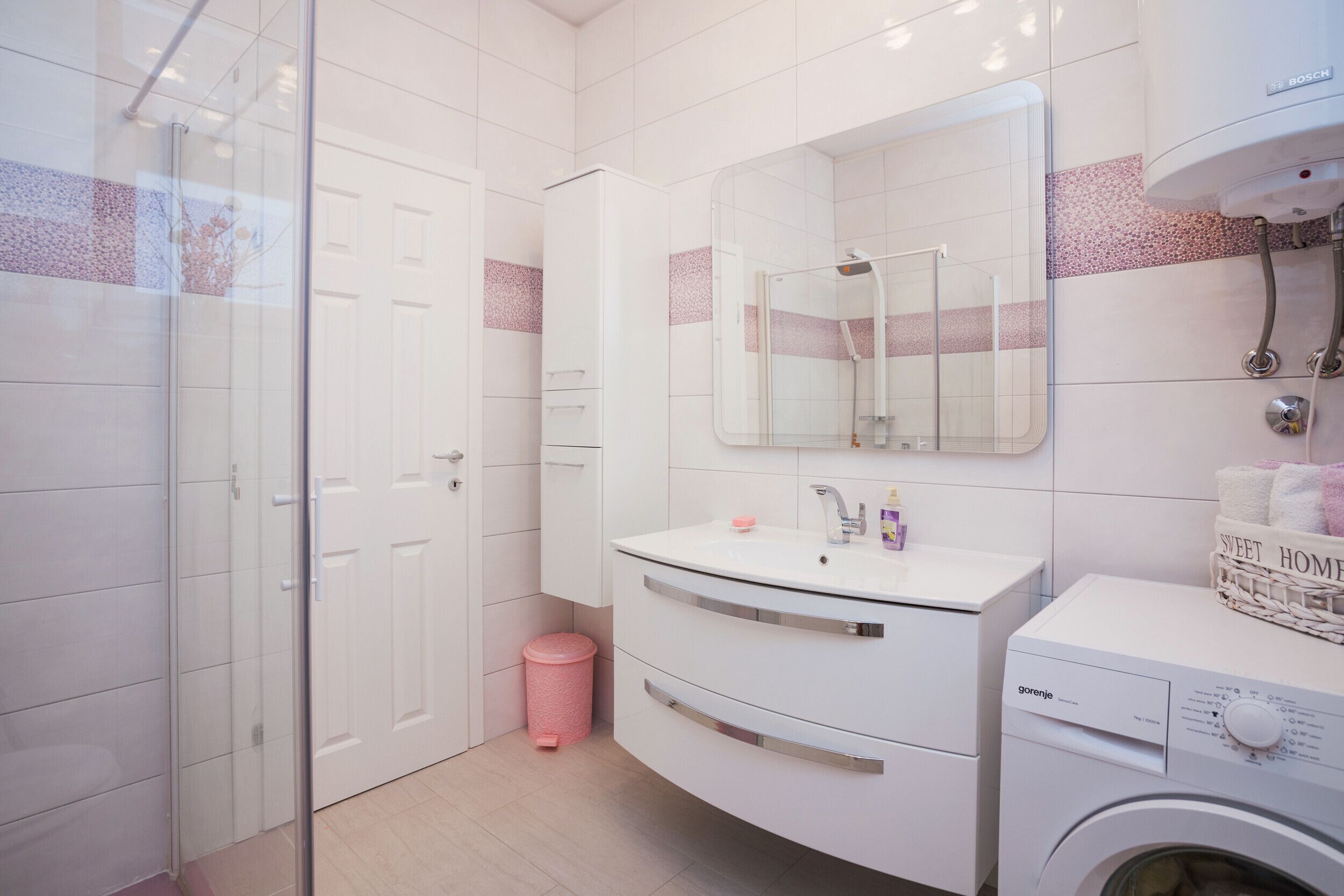 Een moderne badkamer met een douchecabine van glas, een witte wastafel met spiegel erboven en een wasmachine.