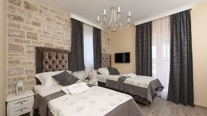Quarto de hotel com duas camas, parede de pedra, lustre e televisão.