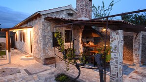 Ein Steinhaus mit Ziegelkamin, einer Pergola und einem kleinen Garten mit einer Weinrebe.