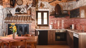 Eine rustikale Küche mit Kamin aus Ziegelsteinen, Holzschränken und einem Essbereich mit Tisch und Stühlen.