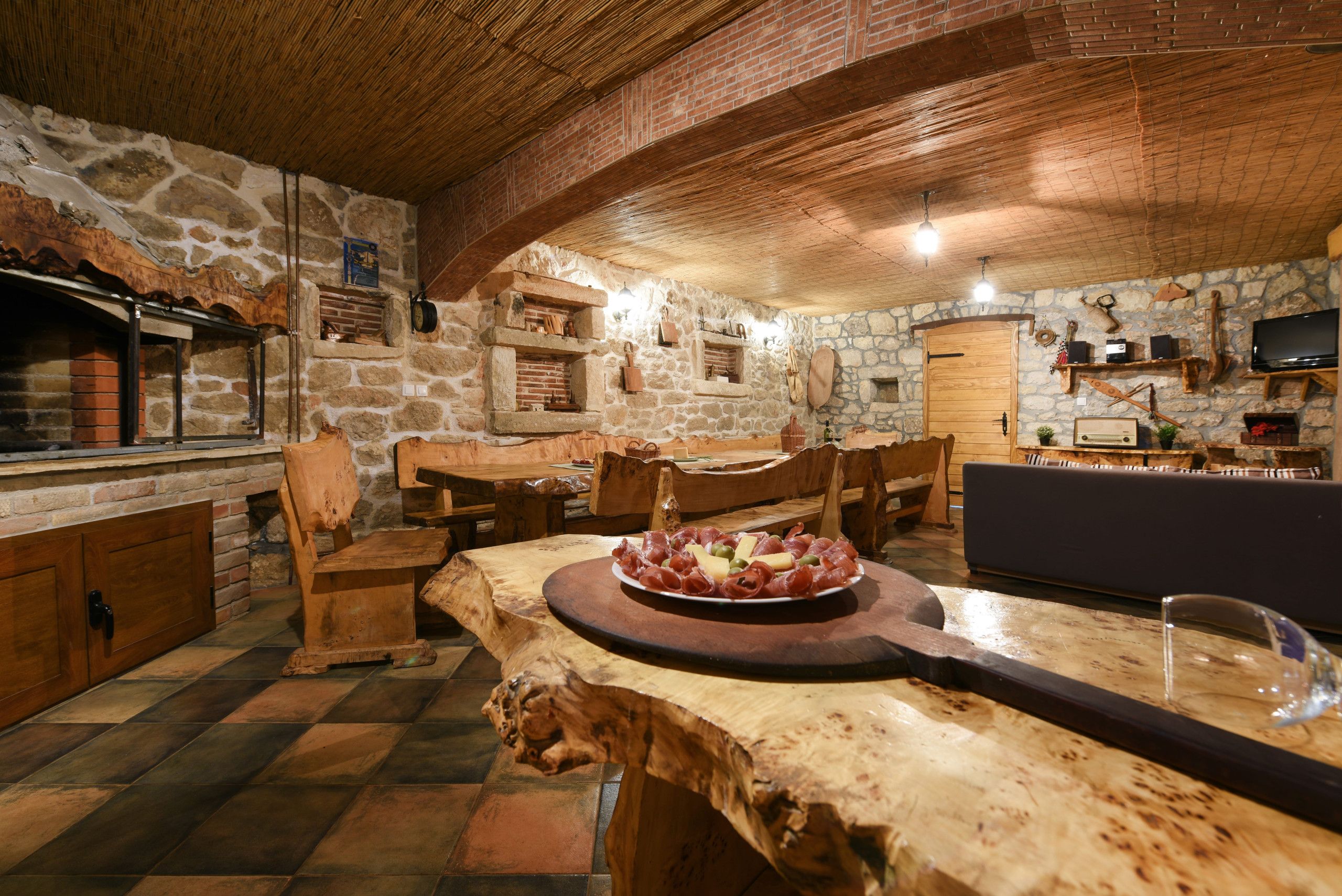 Interior rústico em pedra com mesa de jantar de madeira, cadeiras e lareira de pedra.