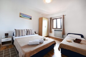 A hotel room with two beds, a nightstand, a lamp, a painting, a window with curtains, and a radiator.