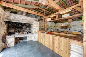 Una cocina rústica con chimenea de piedra, vigas de madera y piso de baldosas.