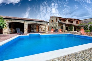Un área de piscina con edificios de piedra, mobiliario exterior y cielo despejado.