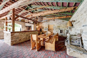 Un interior con pared de piedra, vigas de madera, suelo de ladrillo y una mesa de madera con sillas.