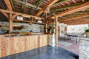 A rustic kitchen with stone walls, wooden beams, and a tiled floor.
