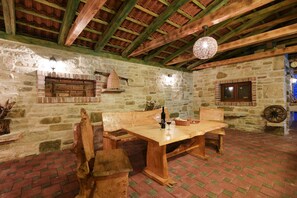 A rustic stone interior with a wooden table and benches, a hanging light fixture, and a brick fireplace. - Villa Smilje (Posedarje)