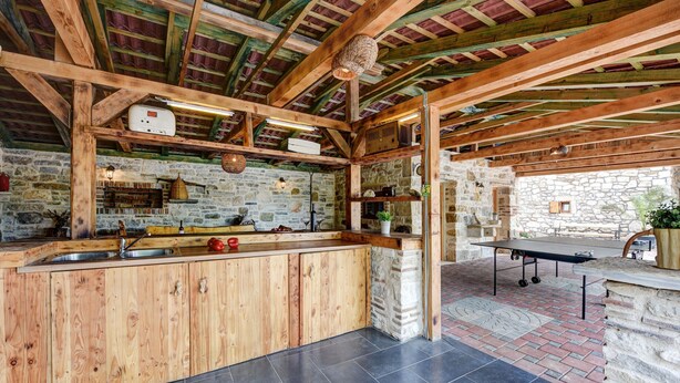 A rustic kitchen with wooden beams, stone walls, and a ping pong table. - Villa Smilje (Posedarje)