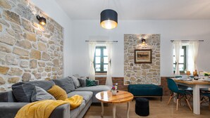 Uma sala de estar acolhedora com uma parede de pedra, um sofá cinzento, uma mesa de centro de madeira e uma área de jantar com mesa e cadeiras.
