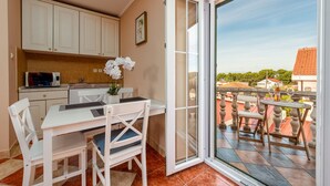 A kitchen with white cabinets and a microwave, a dining area with a table and chairs, and a balcony with outdoor seating. - Villa Stocco (Preko)
