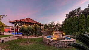A gazebo with a tiled roof, a stone fountain, and a pool in a landscaped garden. - Villa Stocco (Preko)