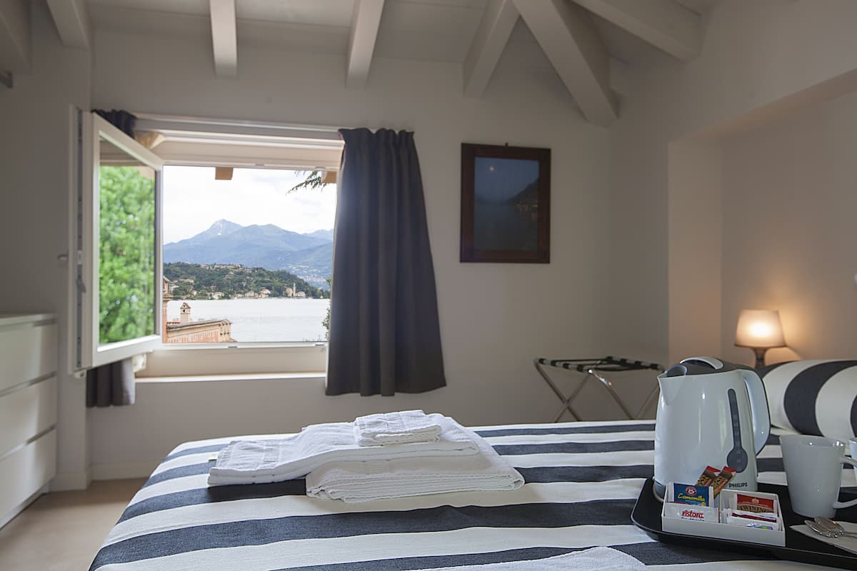 Une chambre d’hôtel avec un lit, une fenêtre avec des rideaux, une vue sur les montagnes, une bouilloire, une tasse et un plateau avec des articles de toilette.