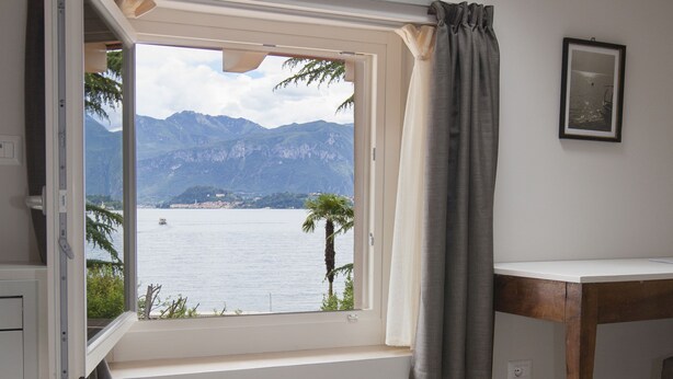 A bedroom with a bed, a desk, and a window with a view of a lake and mountains. - Balbianino (Tremezzina)