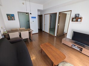 A modern living room with a sofa, a wooden coffee table, a TV, and a dining area with a table and chairs.