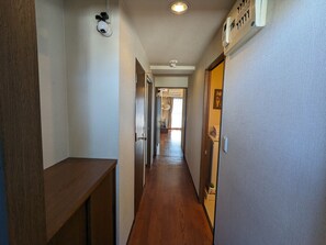 A hallway with wooden flooring, a white wall with a textured pattern, and a door with a small window.
