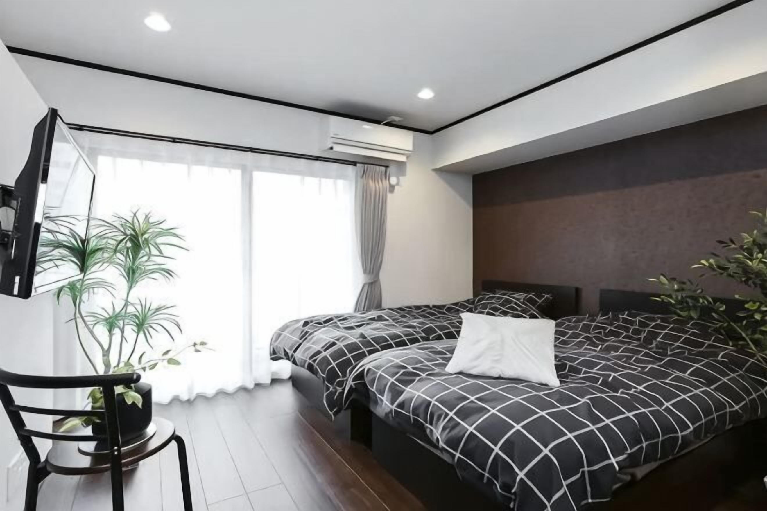 Quarto moderno com duas camas, uma janela grande e uma planta em vaso.