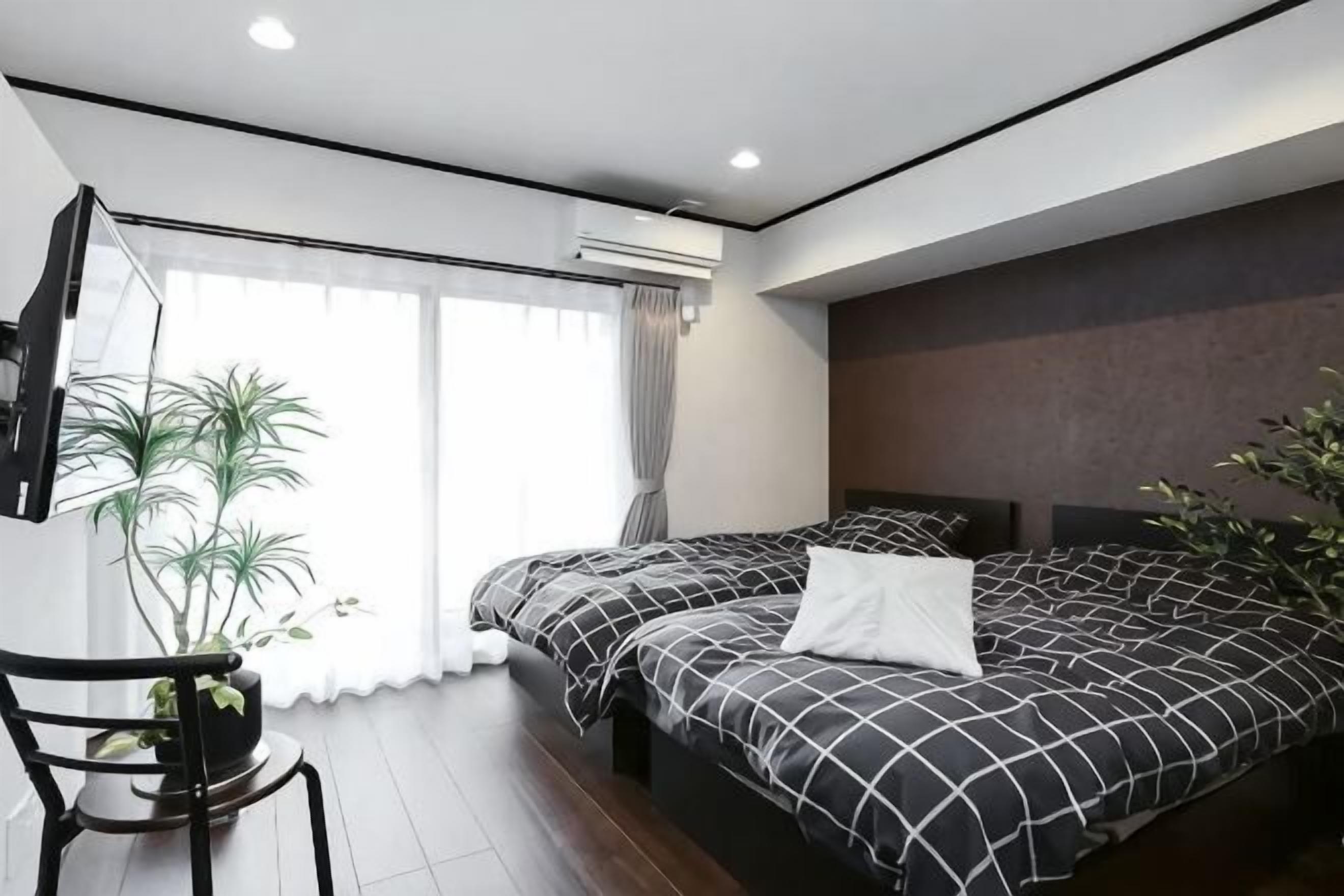 A modern hotel room with two beds, a large window, a potted plant, and a flat-screen TV.