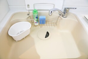A bathroom sink with a white basin, a metal soap dish, a green bottle, and a blue sponge. - Mina Aoi Apartment (Nagoya)
