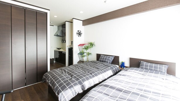 A modern bedroom with two beds, a kitchenette, and a sliding door closet. - Mina Aoi Apartment (Nagoya)
