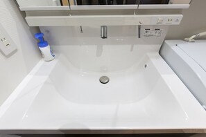 A white bathroom sink with a chrome faucet, a soap dispenser, and a mirror above it. - Mina Aoi Apartment (Nagoya)