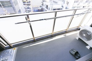A balcony with a view of a parking lot, a fan, and a pair of slippers. - Mina Aoi Apartment (Nagoya)
