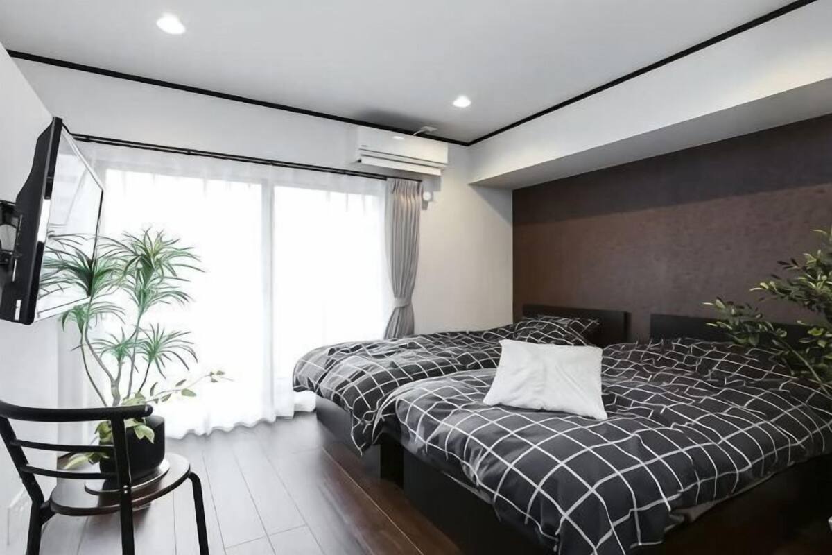 A modern bedroom with two beds, a large window, and a potted plant.