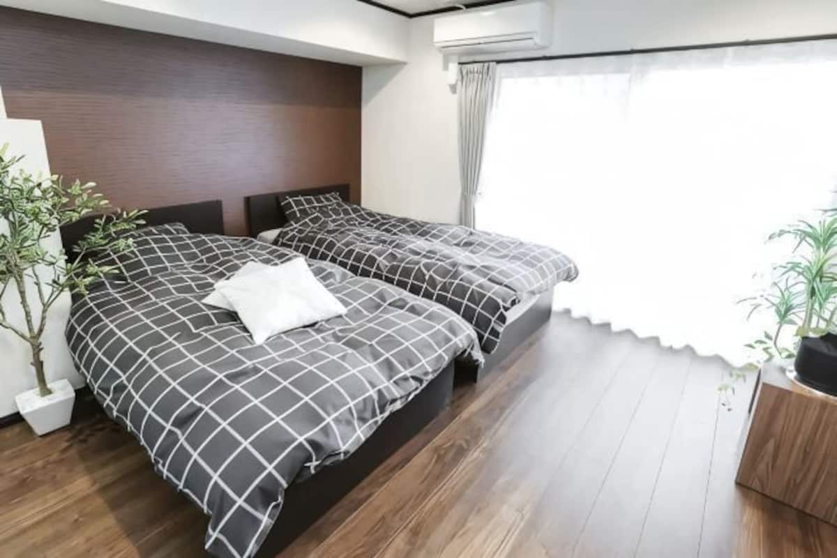 A hotel room with two beds, a wooden floor, a potted plant, and a window with curtains.