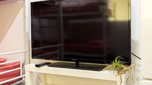 Un televisor de pantalla plana sobre un soporte blanco, con un control remoto y una pequeña planta al lado.