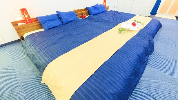 Una cama bien hecha con ropa de cama azul y beige, un cabecero de madera y un objeto decorativo rojo sobre la mesita de noche.
