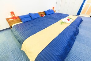 Una cama bien hecha con ropa de cama azul y beige, un cabecero de madera y un objeto decorativo rojo sobre la mesita de noche.