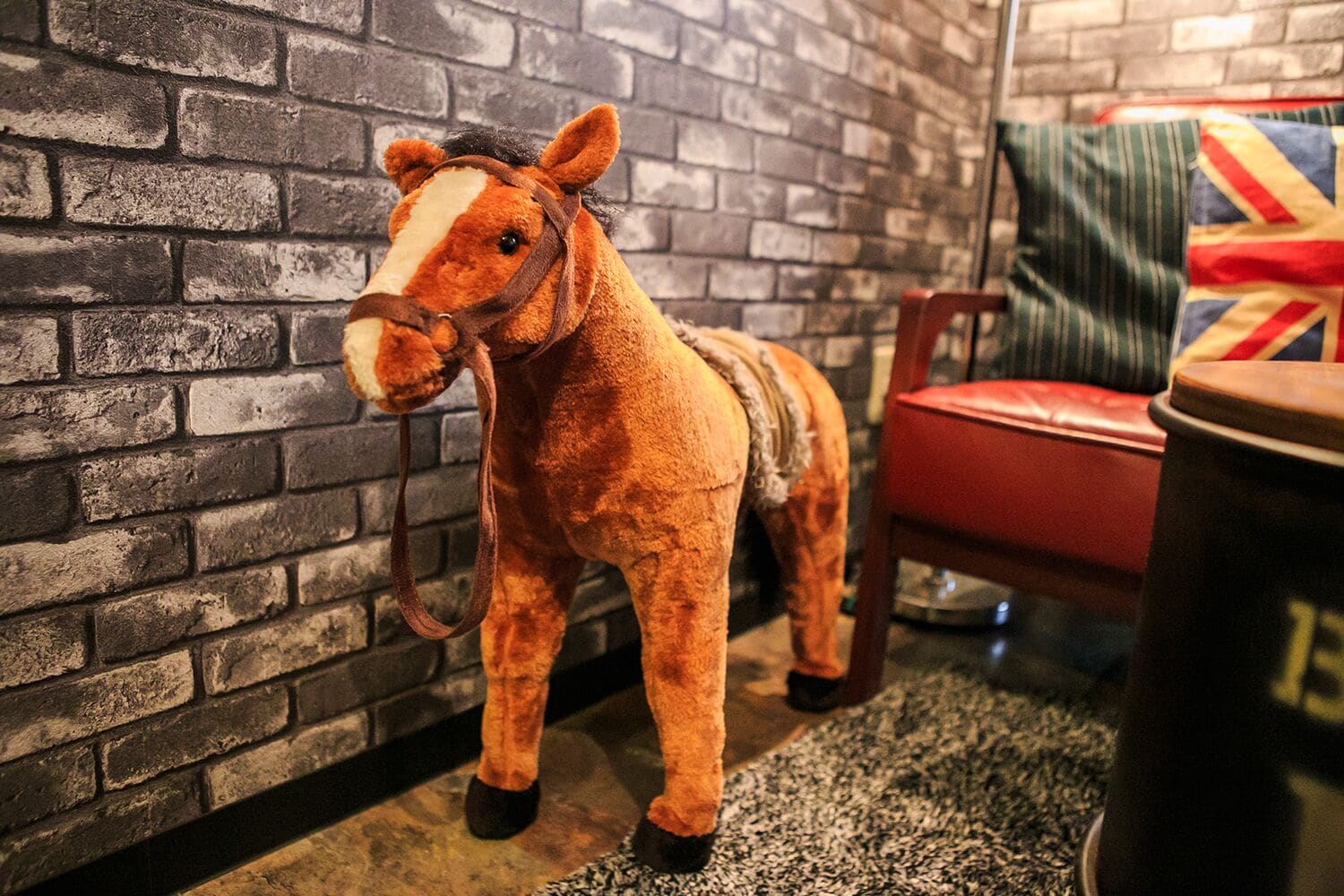 A plush toy horse in a room with a brick wall and a red chair.