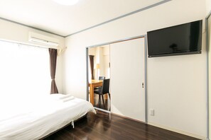 A bedroom with a bed, a desk, a chair, a TV, and an air conditioning unit.