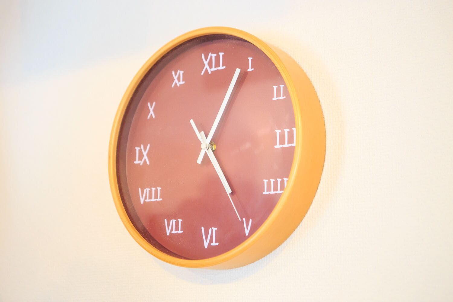 Une horloge murale ronde, avec des chiffres romains et un cadre jaune.