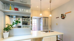 A modern kitchen with white cabinetry, a central island with a sink, pendant lighting, and a potted plant. - Casa de Marzo (Nagoya)
