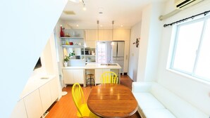 A compact kitchen with white cabinets, a dining table with yellow chairs, and a white sofa. - Casa de Marzo (Nagoya)