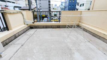 A rooftop terrace with a metal clothes drying rack, concrete floor, and a view of a cityscape with buildings and a yellow taxi in the background.
