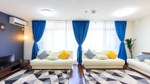 A modern living room with two sofas, a flat-screen TV, and a large window with blue curtains. - Dai 40 prosper Apartment (Nagoya)